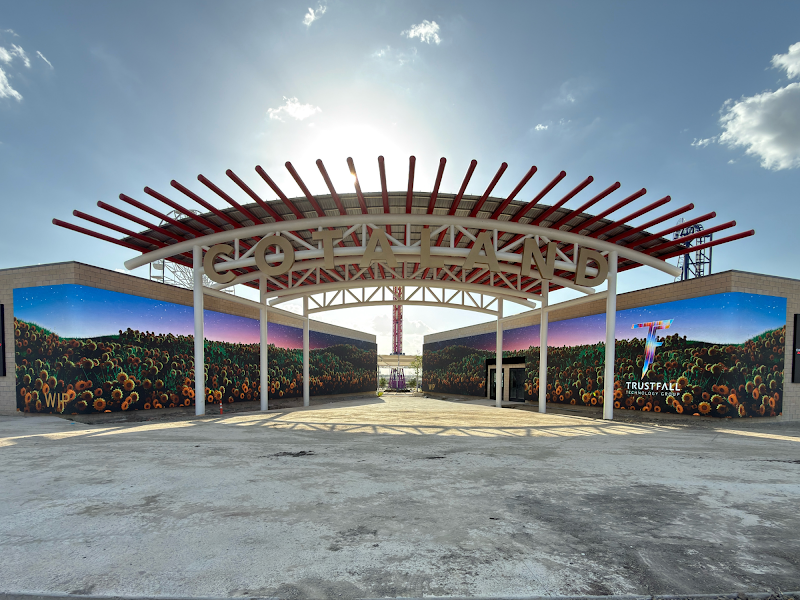 Large outdoor LED video walls displaying a sunflower field beneath an arched steel canopy, with Trust Fall Technology Group branding